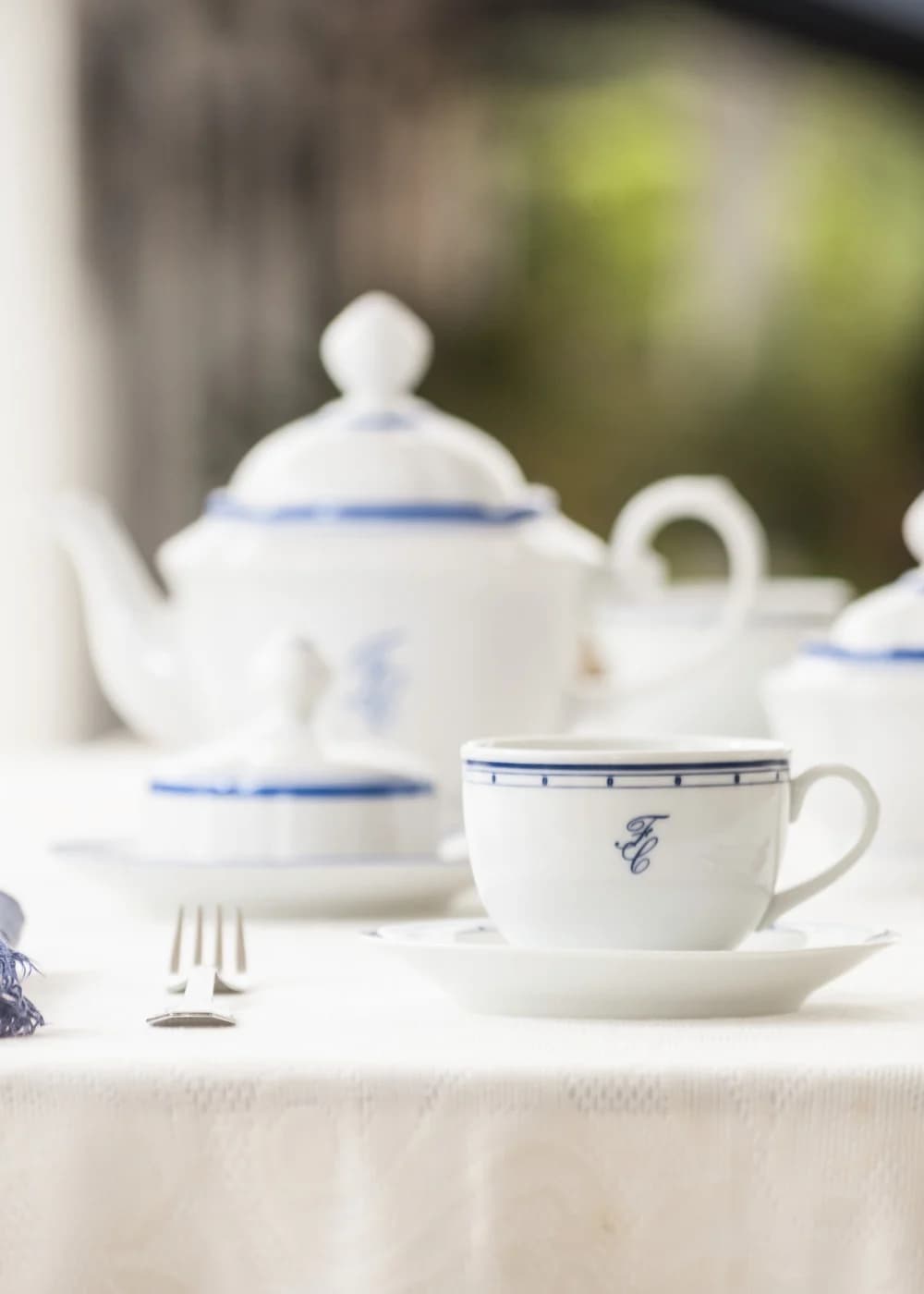 Xícara branca com monograma azul, em uma mesa posta para café